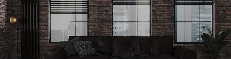 Black Venetian blinds raised above three windows in a brick-walled living room