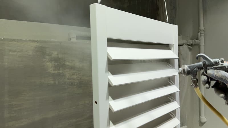 A white louvred shutter panel being spray-finished in the paint booth